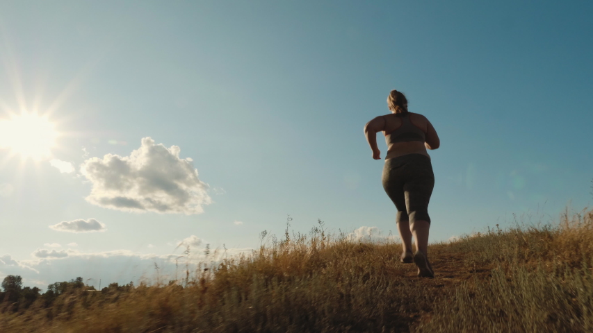 Rear view: Young plus size girl runs up the hill in the early morning. Concept of losing weight with exercise for health. Slow-motion shot