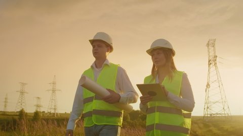 Coworking engineers with tablets on solar plant. Adult men and women in hardhats using tablets while standing outdoors on transformer platform. Transportation of clean energy