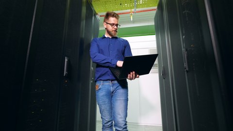 IT specialist with a laptop is observing server blocks. Server Engineer Working at Data Center