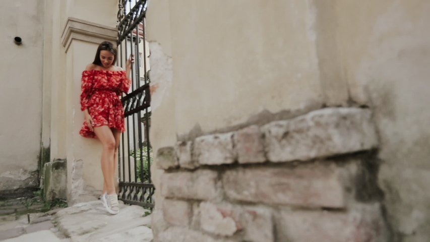 Happy Young Woman With Charming Cheerful Face Having Fun On Street Of Old Town. Millennial Girl Travels To Old Town During Student Vacation Holidays. Attractive Woman Posing Near Gate Of Building.
