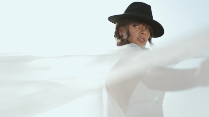 Close-up Of Attractive Bride In White Wedding Dress And Black Floppy Hat. Fashion Model Posing In Nature. Stylish Woman, Elegant Dress, Happy Romantic Holiday, Blowing Clothes, Feminine Concept.