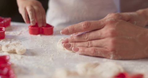 Portrait of little boy's and his mother's tidy hands which cuts the dough with mold. Young mother is cooking in the kitchen with her son, dirty hands, make the dough for baking. 4K video