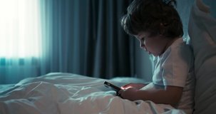 Young pretty boy sitting in white bed and search something on the phone. 4K video