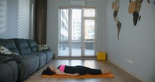 Concentrated attractive young woman wearing leggings and top doing yoga asanas to develop balance, sitting on a mat in living room at home. Cozy spacious room and pleasant atmosphere. 4K video