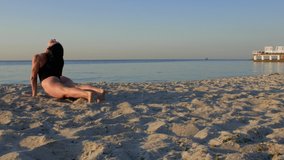 sporty brunette in black body doing yoga exercises on the seashore. fitness, sport, yoga and healthy lifestyle concept. 4k. 4k video