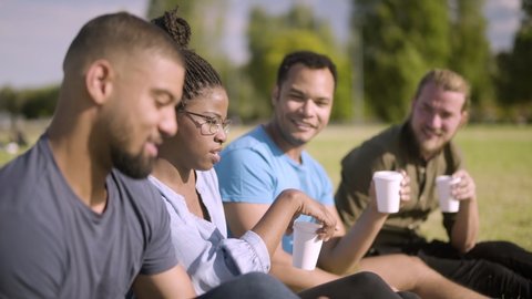 Smiling colleagues sitting on lawn and drinking coffee. Cheerful young people having lively conversation during coffee break. Communication concept