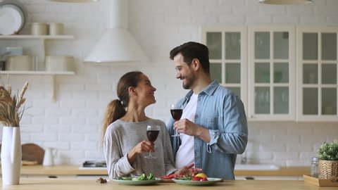 Happy romantic family couple enjoy cooking talking clinking wine glasses together in kitchen, affectionate smiling husband and wife cut healthy vegetable salad celebrate. Body art heart and circle
