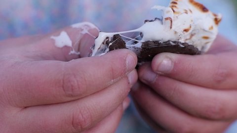 
Kid breaks marshmallow into two parts with fingers slow motion shot. This hand held close up slow motion clip shows girl’s hands separating s’more into 2 parts. 