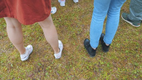 Two girls dance at an open-air concert, stamping their feet on grassy ground. Close view of the legs.