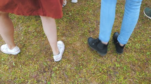 Two girls dance at an open-air concert, stamping their feet on grassy ground. Close view of the legs. Slow motion.