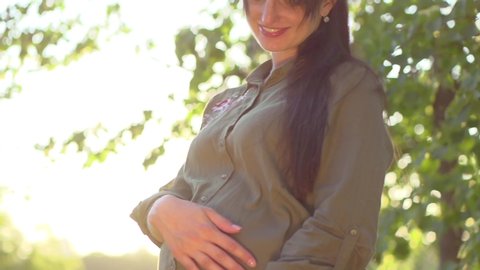 Pregnant Happy Woman outdoors enjoying nature, holding and playing with Baby Shoes in Hands. Mom Expecting her Baby. Pregnant Woman Belly. Pregnancy. Maternity concept. Baby Shower. Slow motion 4K