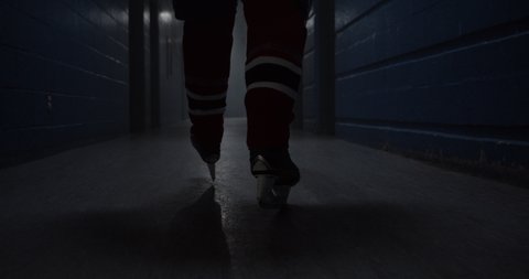 A hockey player walks down a hallway with intensity towards hockey arena featuring his hockey skates, building drama.