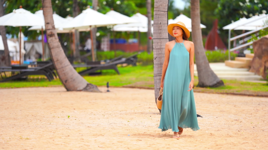 Beautiful happy young Asian woman in long summer dress and hat walking along a tropical beach Royalty-Free Stock Footage #1034402255