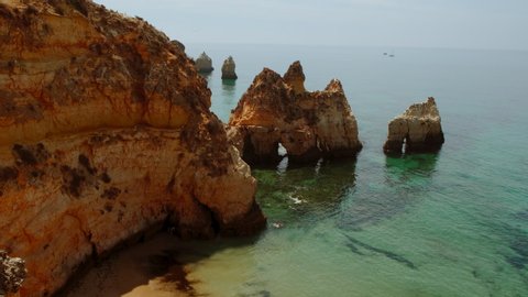 Establishing aerial wide view of pristine waters and beautiful rock formations in Tres Irmaos Beach in Alvor, The Algarve, Portugal