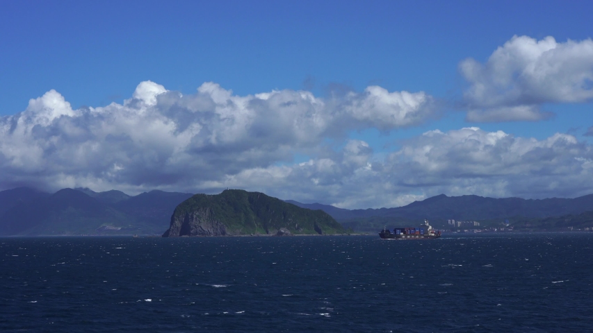 large container ship transports colored containers on waves of Pacific Ocean. container ship on the background of desert mountain island in Pacific Ocean on clear day against the blue sky with clouds