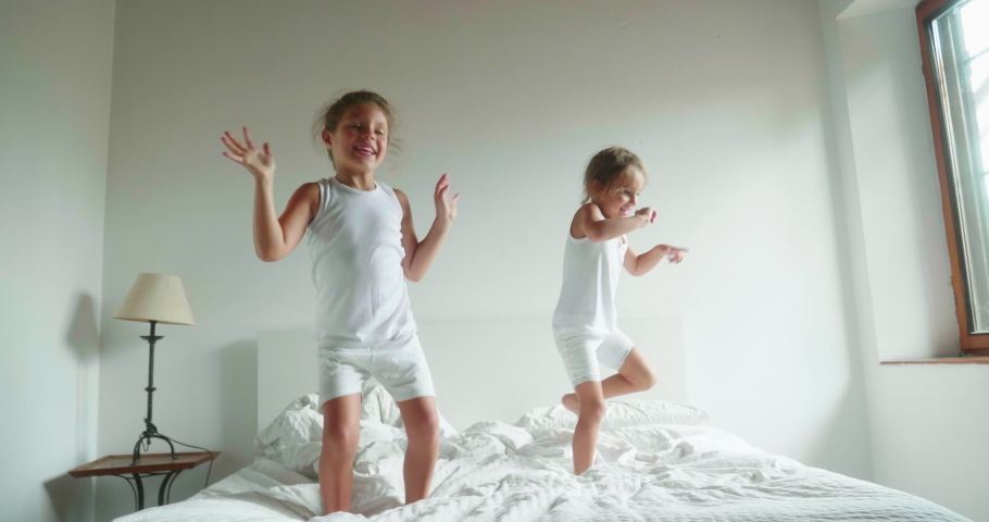 Authentic slow motion shot of two little girls sisters in white pajamas are having fun to jump on the bed of their parents bedroom. Royalty-Free Stock Footage #1034427590
