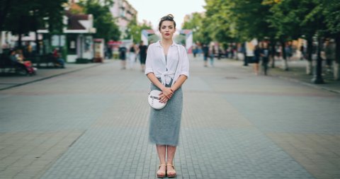 Time lapse of attractive adult woman standing in city center in busy street looking at camera wearing casual clothes while crowds of people are walking by.