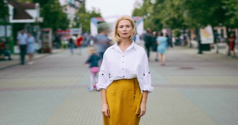 Time lapse portrait of beautiful mature lady with serious face in city street standing alone looking at camera. Summer town, people and modern life concept.