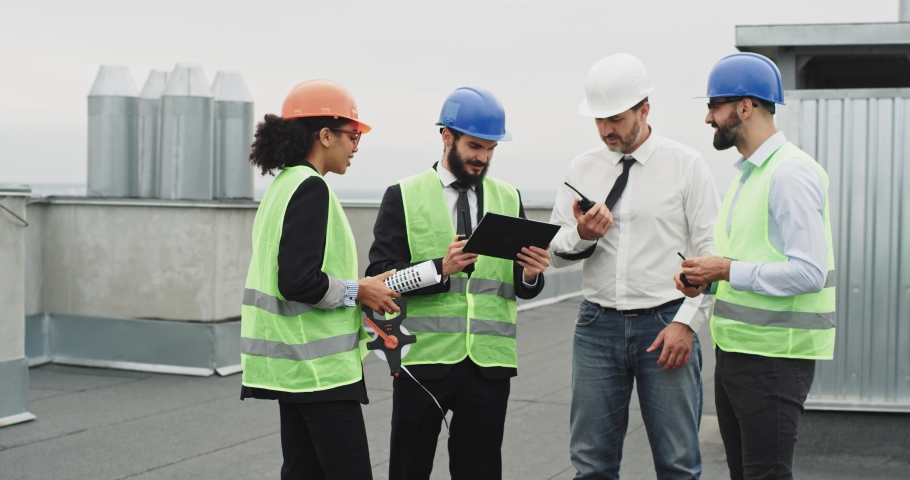 On the rooftop of construction site group of engineers and architect holding the measurement and some notes of building they wearing helmets analyzing all together the plan