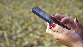 Closeup view of white woman holding smartphone in hands. Person browsing internet social media resources standing outdoors in sunny autumn park. Real time 4k video footage.