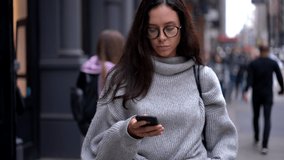 Attractive female tourist in trendy apparel walking around city downtown using cellphone device for tracking gps destination via location application, beautiful millennial sending sms message