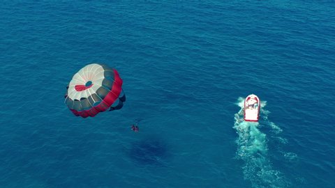 Aerial view. People flying on a colorful parachute towed by a motor boat. Parasailing in blue sky.