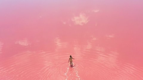 young woman going into the lake with brigth pink water. Unique amazing landscape.