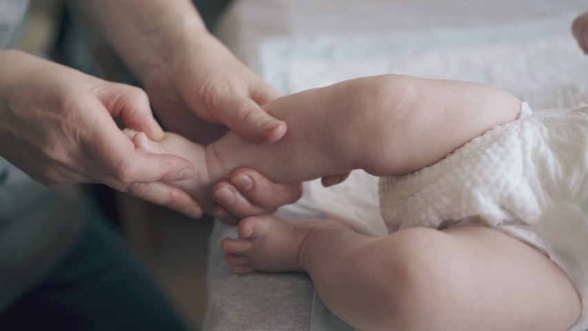 Infant boy in white diaper lies on baby changing table and skilled nurse performs hypertonus legs foot massage closeup | Shutterstock HD Video #1034444081