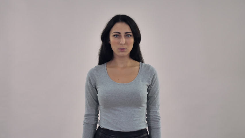 afraid adult mixed race caucasian woman with black straight hair showing feeling fright. Portrait woman wearing casual grey shirt posing in studio on background