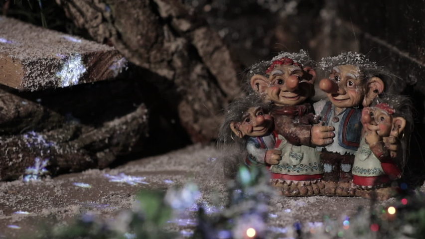 Fairytale family of elves and trolls on the background of a wooden house with blinking lights. Copy space.