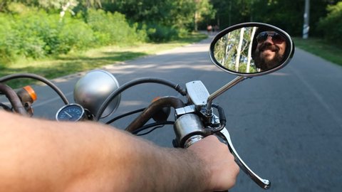 Reflection of a happy man in the mirror of a vintage scooter in the forest road, slow motion. Handsome man rides on a country road at sunrise 4k