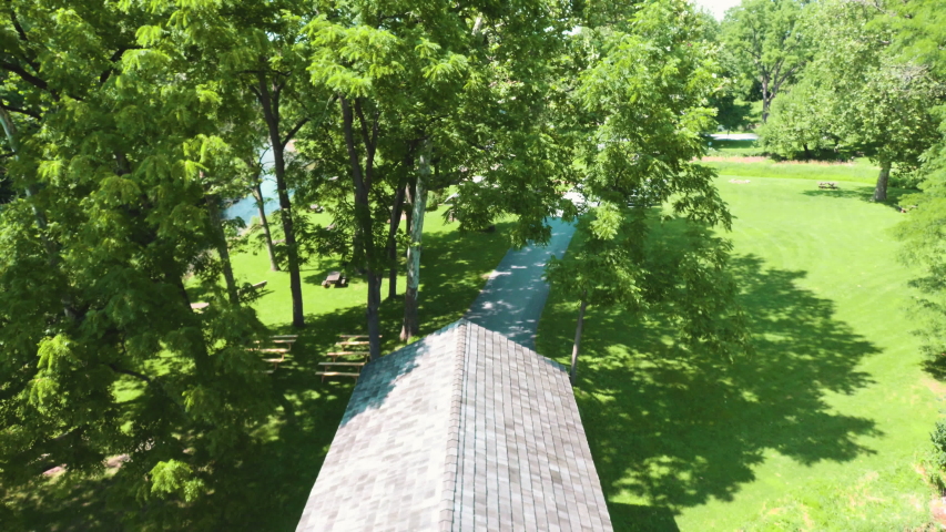 Aerial slowly flying back to reveal covered bridge over stream in rural countryside. 60 frames per second allows for smooth playback or slow motion.