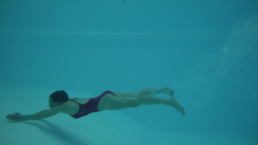 Medium shot of woman swimming underwater in a swimming pool | Shutterstock HD Video #1034456417