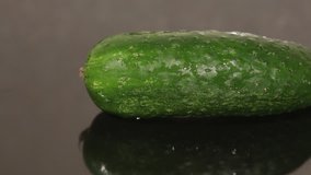 Closeup of a fresh cucumber on a black pan background from a sliding dolly