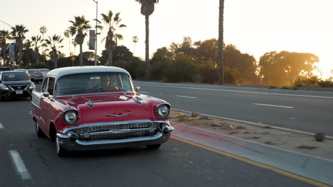San Diego, CA / USA - April 25, 2018: Man Driving Classic Car at Sunset with Palm Trees in Background in Mission Bay