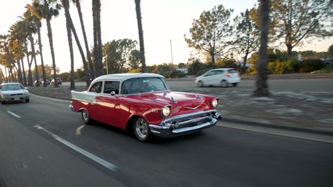 San Diego, CA / USA - April 25, 2018: Wide Shot of Man Driving Classic Car at Sunset in Slow Motion, 1957 Chevy