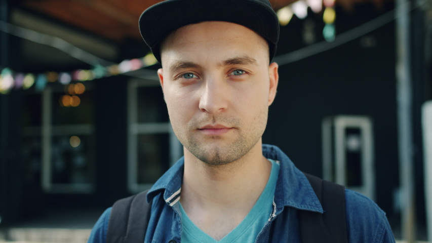 Portrait of handsome guy looking at camera with serious face then smiling standing outdoors in the street. Human emotions, people and urban life concept. Royalty-Free Stock Footage #1034469059