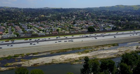 Aerial Drone flying over light traffic on the 91 freeway with Santa Ana River in the foreground and homes in the background in Orange County, California