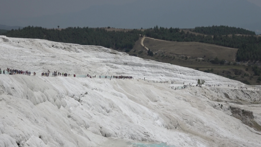 Pamukkale, Denizli, Turkey - 16th of July 2019: 4K Viewing long train of tourists walking on the sinter terraces
