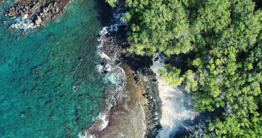 An aerial top down view of waves crashing along the shore off the coast of Maui, Hawaii on a sunny day.