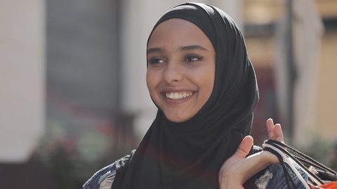 Happy young muslim woman in hijab walking down the street with shopping bags in her hand.