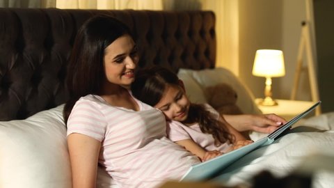 Mother reading bedtime story to her adorable little daughter at home
