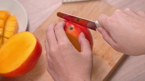 Young woman is cutting a beautiful fresh juicy mango to eat on a wooden table and chopping board in the kitchen, close up , 4K video shot.