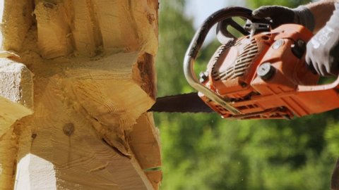A man carves a wooden statue with a chainsaw.