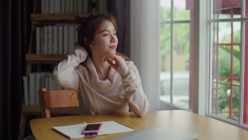 4K locked shot pretty girl wearing winter clothes sitting near window, she stretched out her arms to stretch lazily