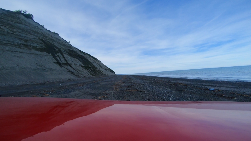 POV over the hood of a red off-road 4x4 vehicle while driving along a desolate beach near Anchor Point, Alaska