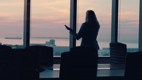 silhouette business woman using smartphone talking to client financial advisor negotiating deal sharing expert advice having phone call working late in office looking out window at sunset