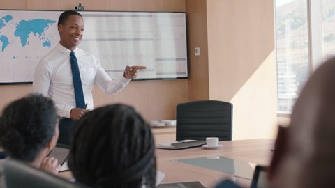 Black businessman presenting financial data on tv screen sharing project with shareholders team leader briefing colleagues discussing company growth ideas in office boardroom presentation