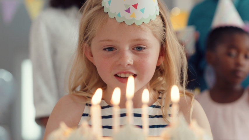 cute birthday girl blowing candles on cake celebrating party with friends happy children having fun celebration at home 4k