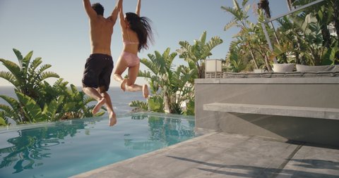 fun couple jumping in swimming pool splashing having fun romantic summer vacation on honeymoon at luxury hotel resort with beautiful ocean view at sunset 4k